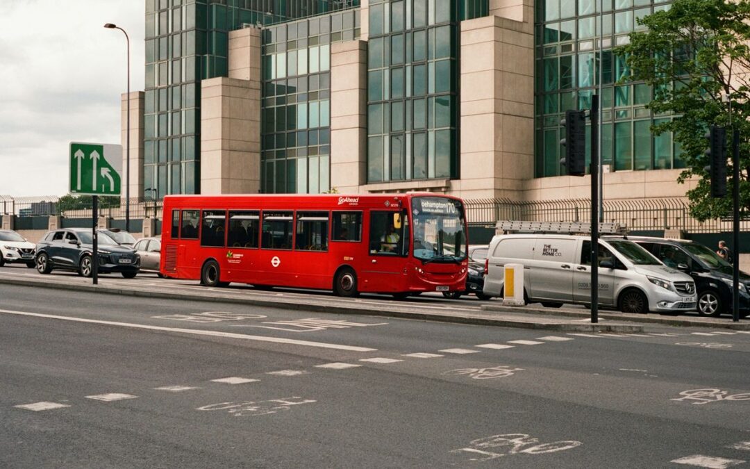 Red bus parked on city street with modern buildings.